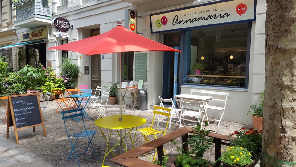 Bistrotische und bunte Stühle vor dem Eiscafé, im Schatten der Platanen