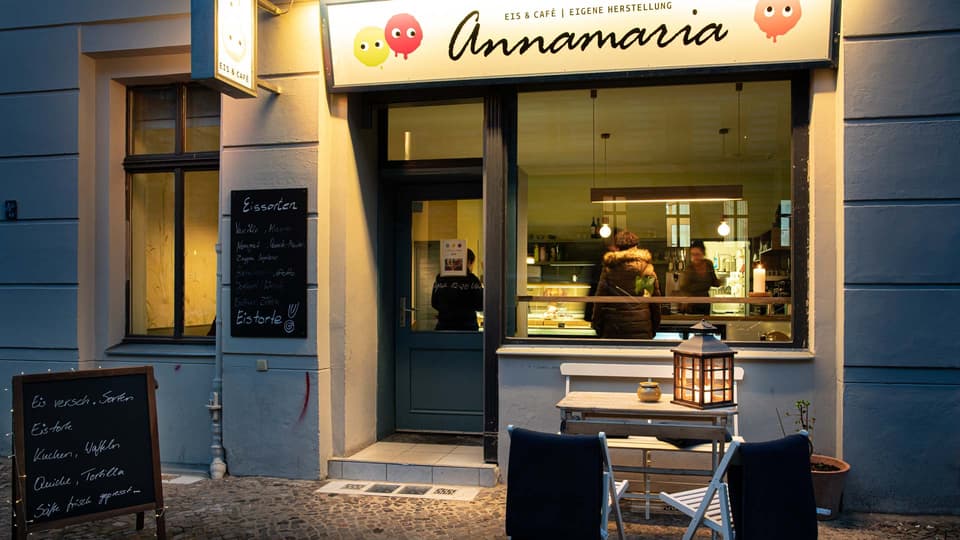 Der beleuchtete Laden am Abend, daneben die Tafel mit den Eissorten