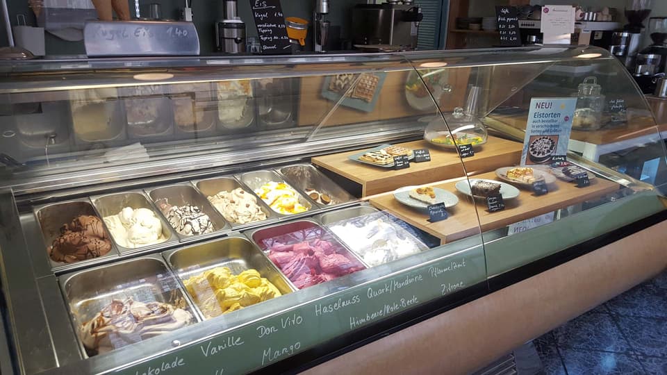 Die Theke mit Eissorten, Kuchen, Waffeln und Quiche; die Sortennamen stehen auf der Glasscheibe